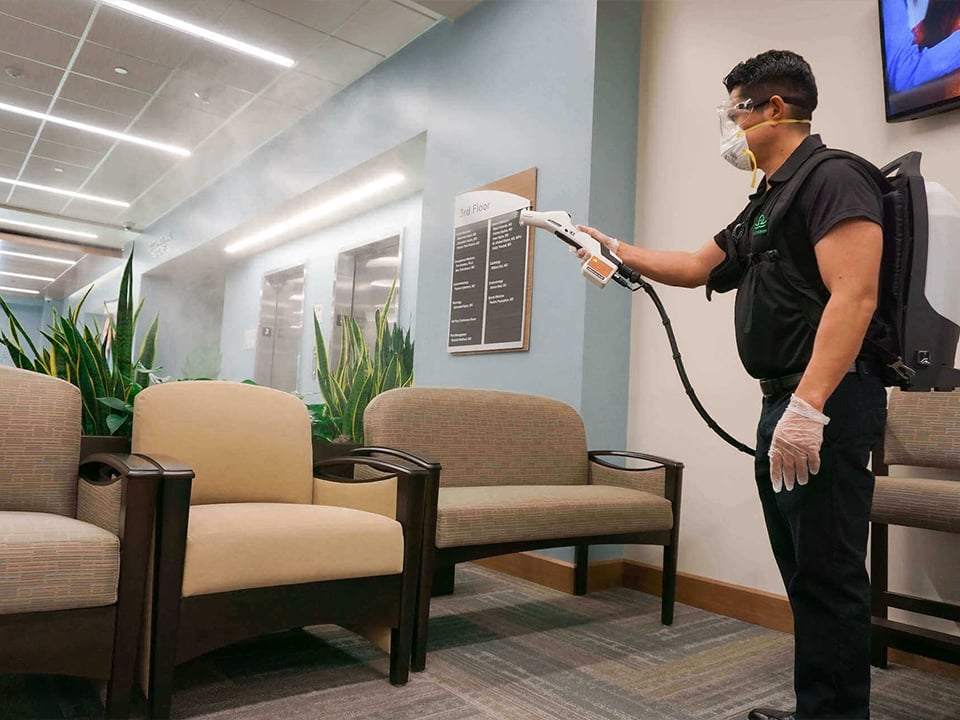 Man in mask uses electrostatic backpack sprayer in waiting room