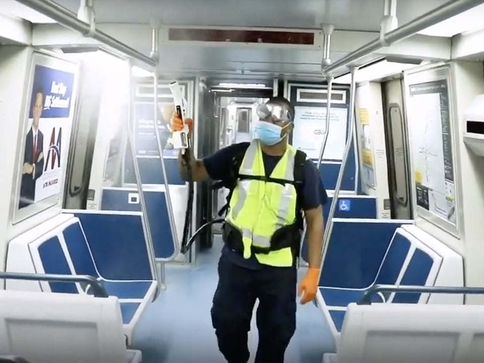 Man in mask and safety mask uses electrostatic sprayer on empty bus