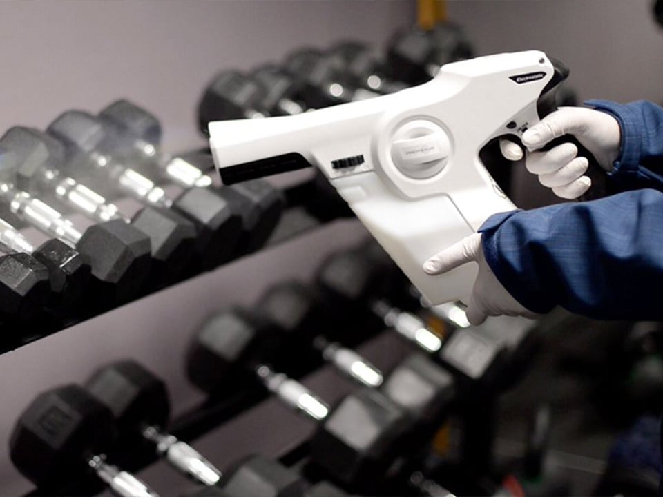 Hands hold electrostatic sprayer over dumbbell weights 