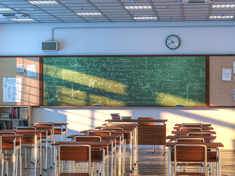 Empty school desks sit in front of chalkboard