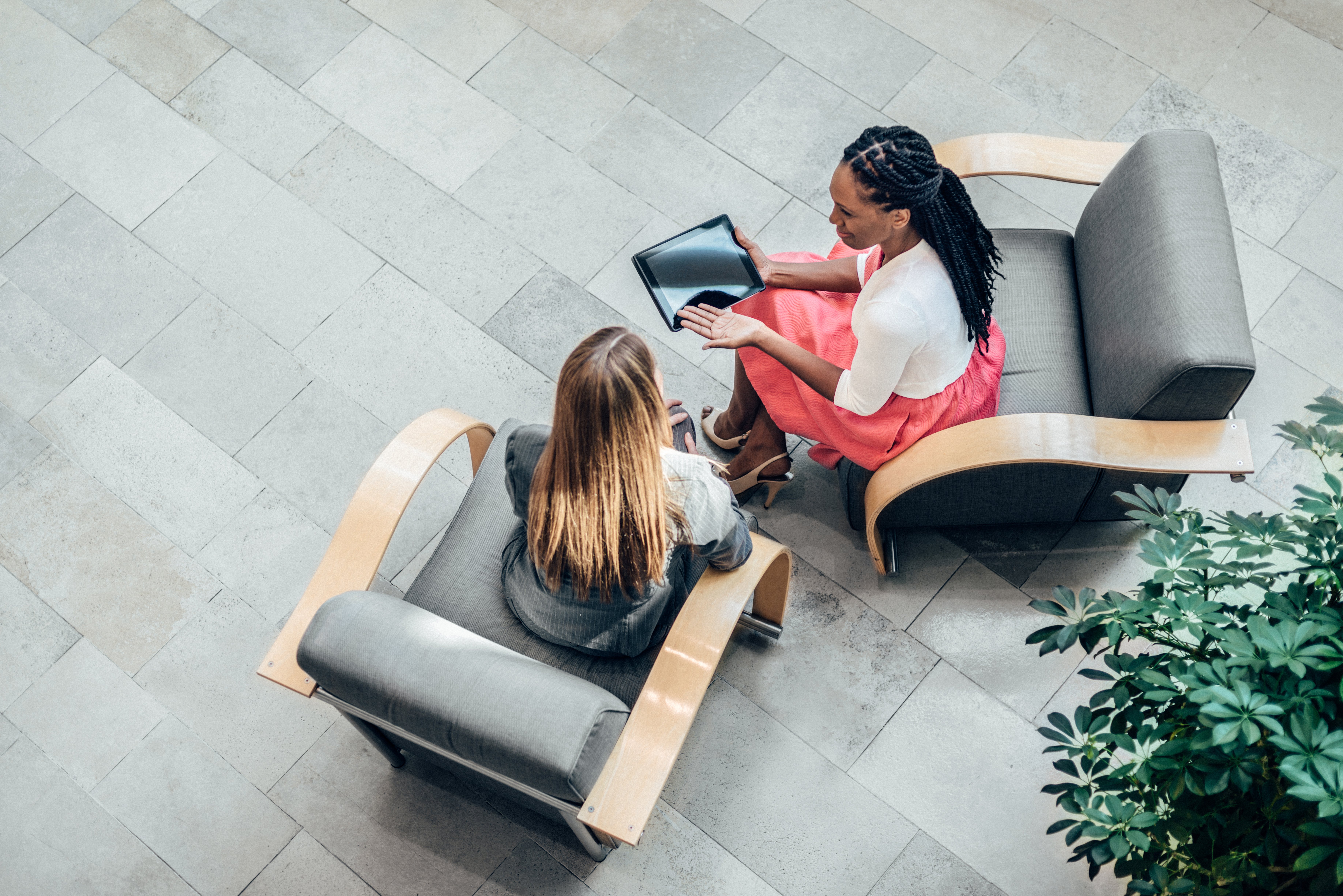 Two women sit in lobby looking at tablet screen