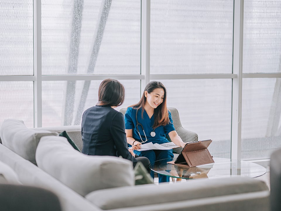 Woman wearing stethescope sits with woman and looks at computer