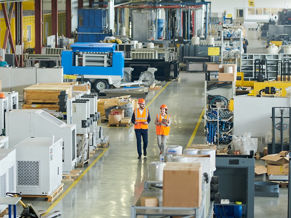 Two works in hard hats and vests walk through factory