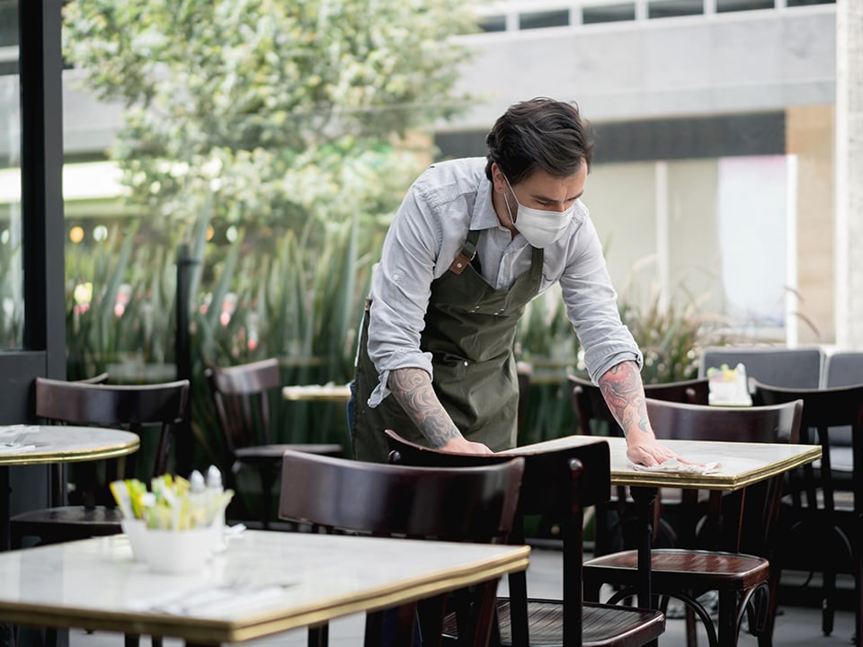 Man in mask wipes restaurant table with rag